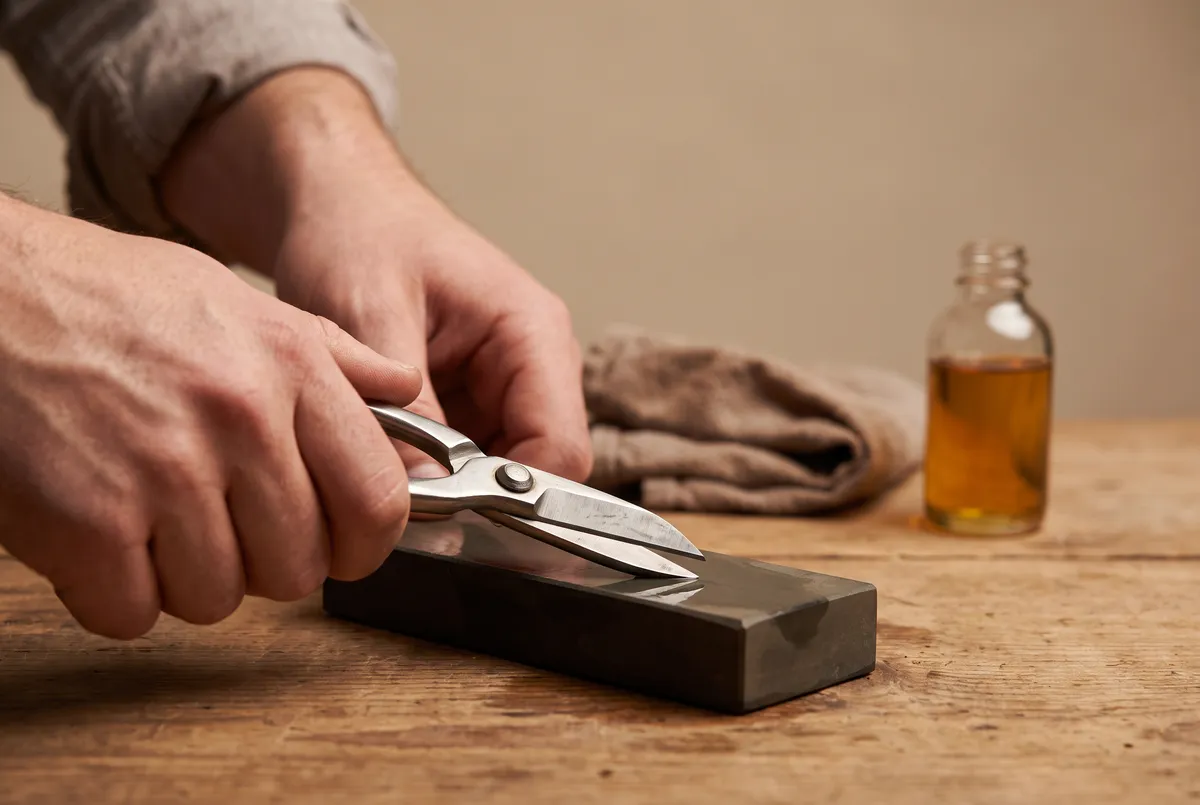 Hands sharpening bonsai shears on a whetstone with the blade held at a steep angle, only the beveled face touching the stone